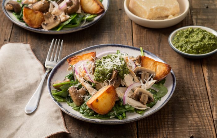 Plate of wilted spinach salad with chicken, potatoes, mushrooms, pesto and Parmesan cheese.