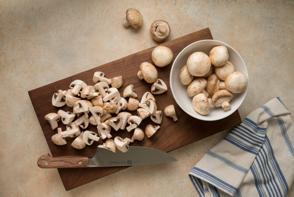 Quartered and whole mushrooms on a cutting board.